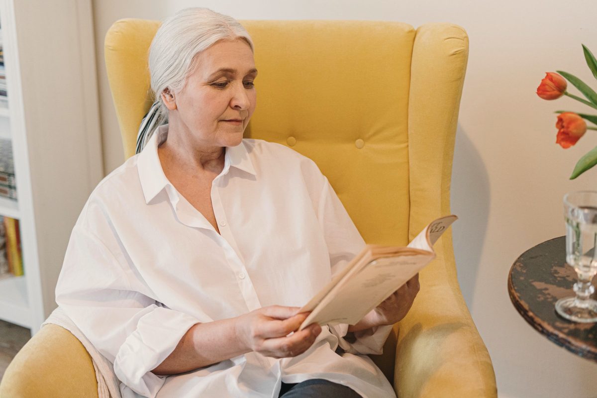 An older woman sitting on a couch reading a book