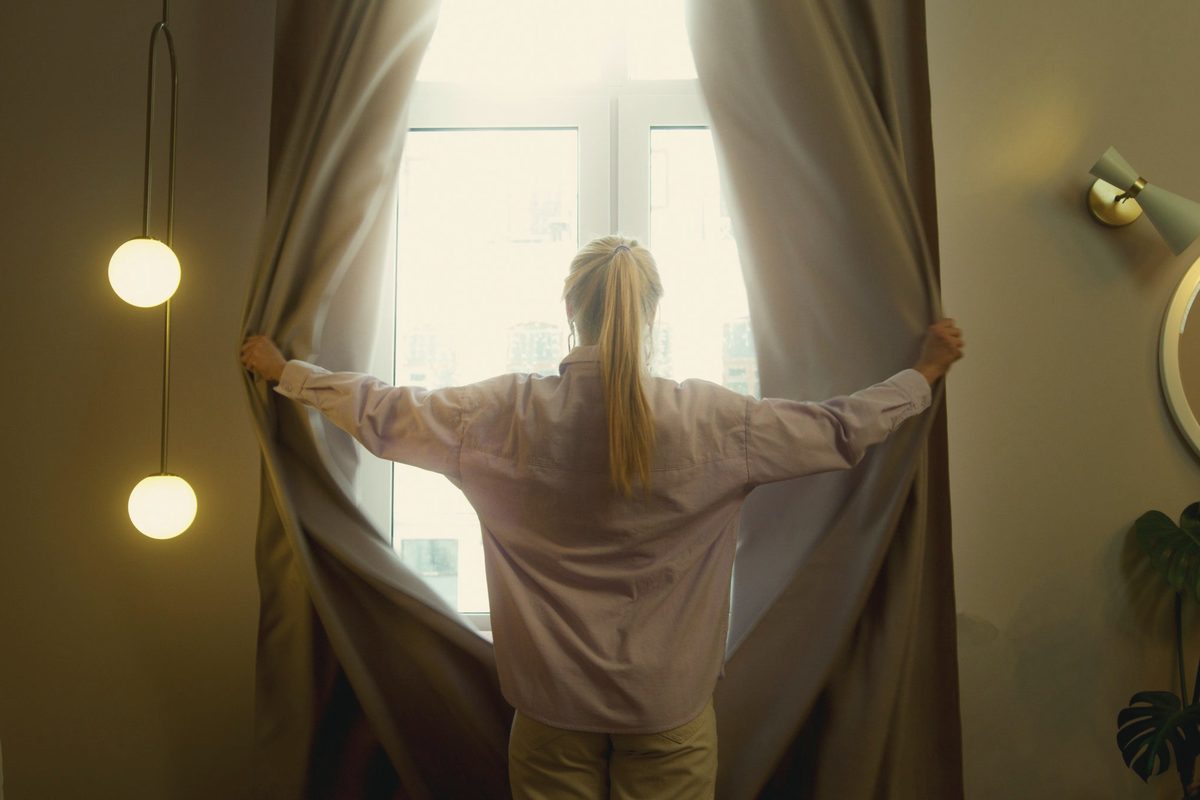 A woman opening the curtains of a window