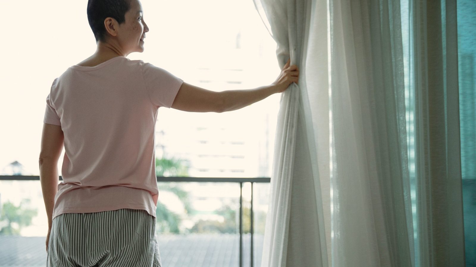 Happy woman with short hair opening curtains of window