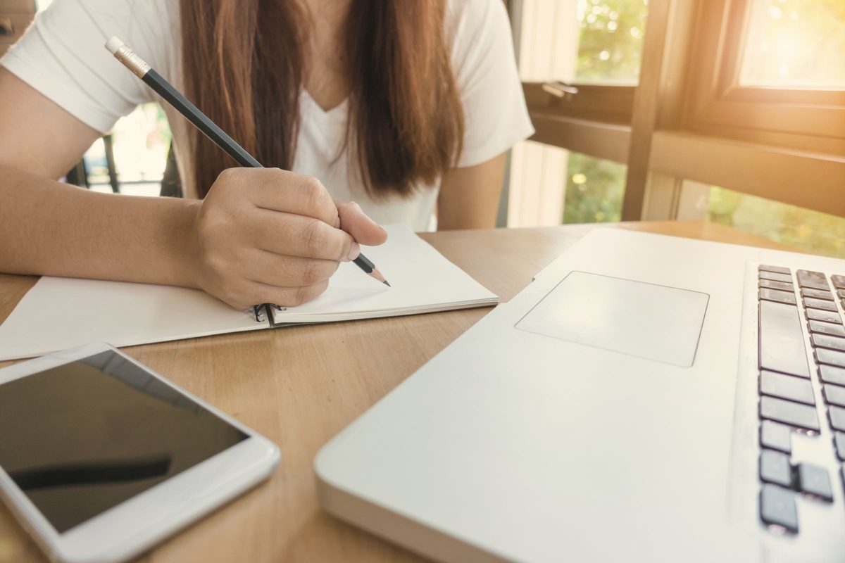 Woman writing in a notebook beside her laptop
