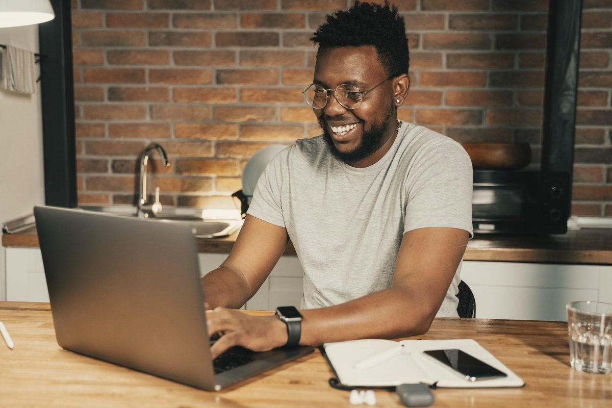 Smiling man working on his laptop at a kitchen bench
