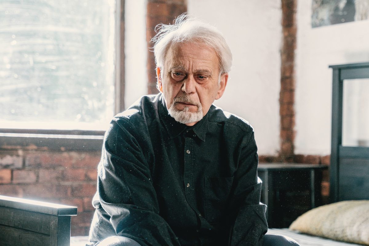 Older man sitting on the edge of a bed