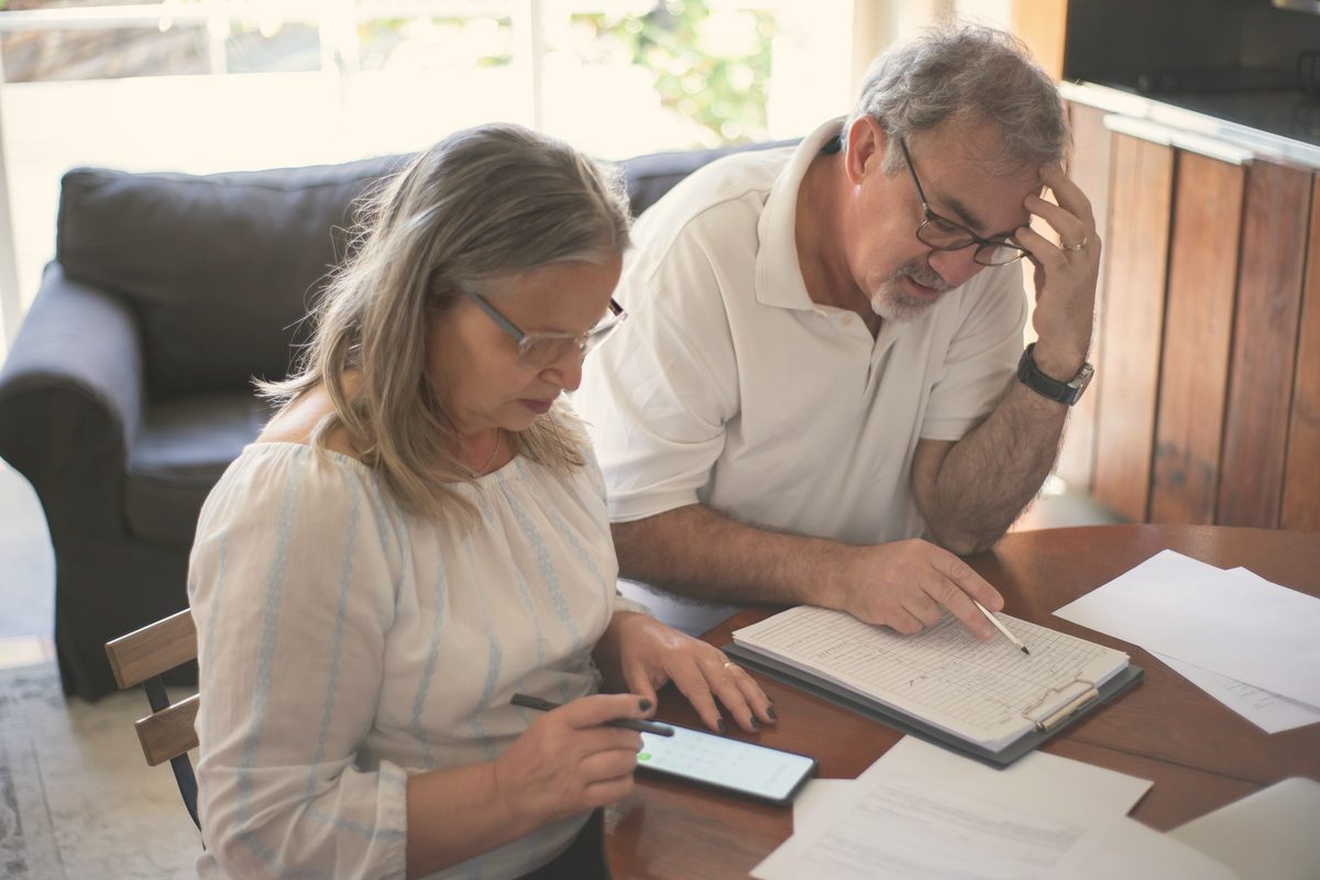 Elderly couple sitting at the table with documents and using a smartphone