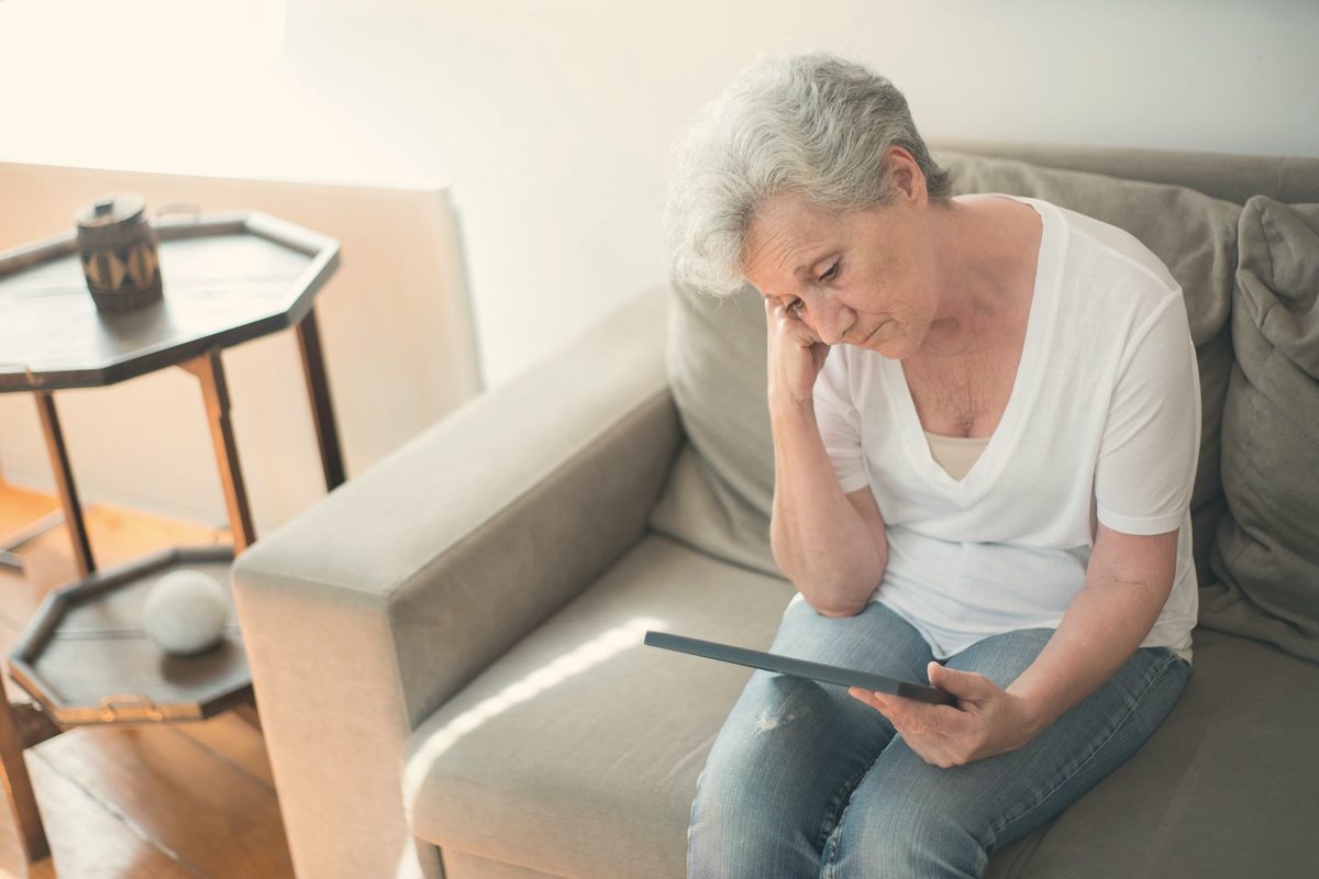 Older woman sitting quietly on a sofa looking at a photo frame