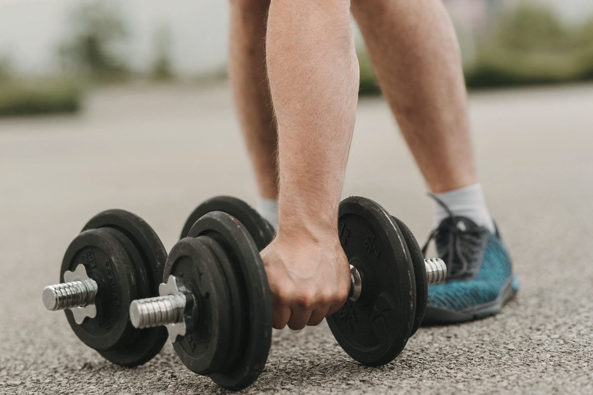 Man lifting a heavy dumbbell on an asphalt road