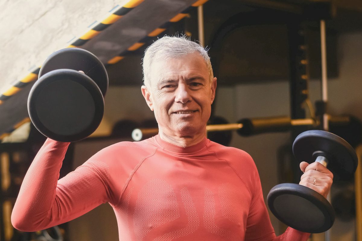Smiling older adult lifting two dumbbells