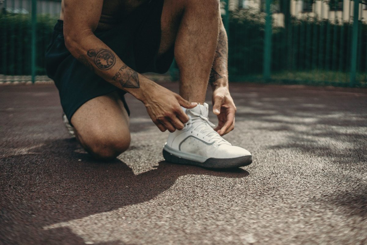 A person kneeling on the ground while tying their shoes