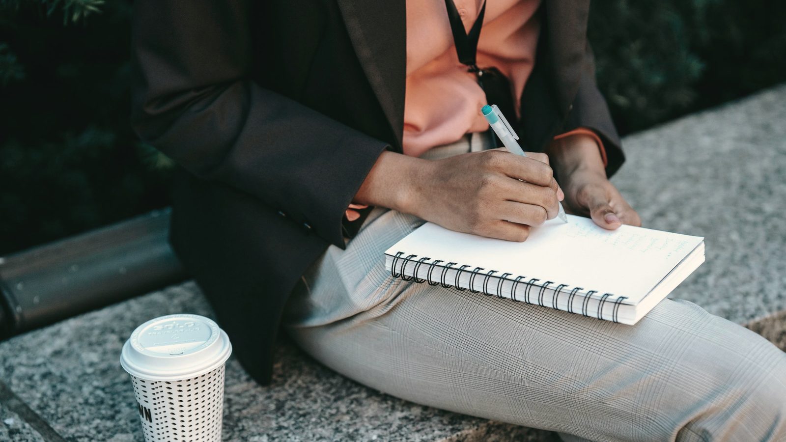 Woman writing notes in planner with takeaway coffee