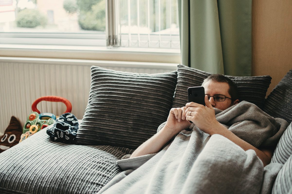Man resting under a blanket on a grey sofa