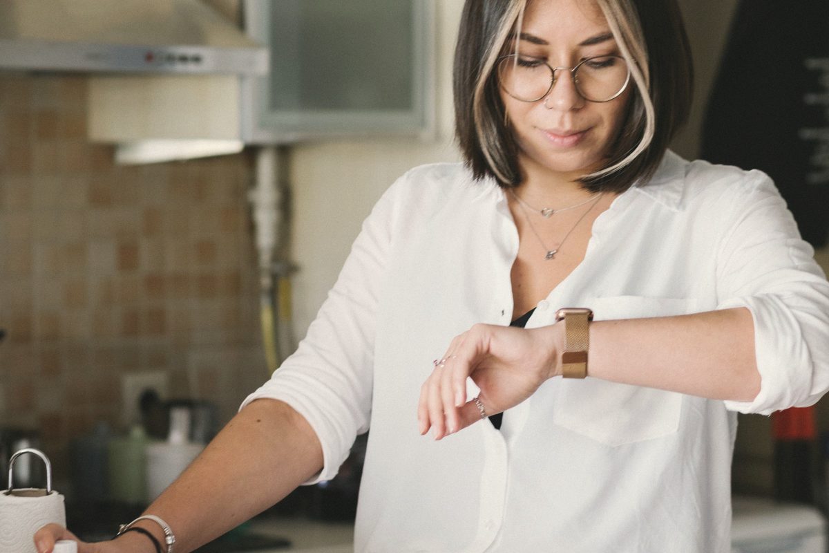 Young woman checking time on wristwatch in kitchen