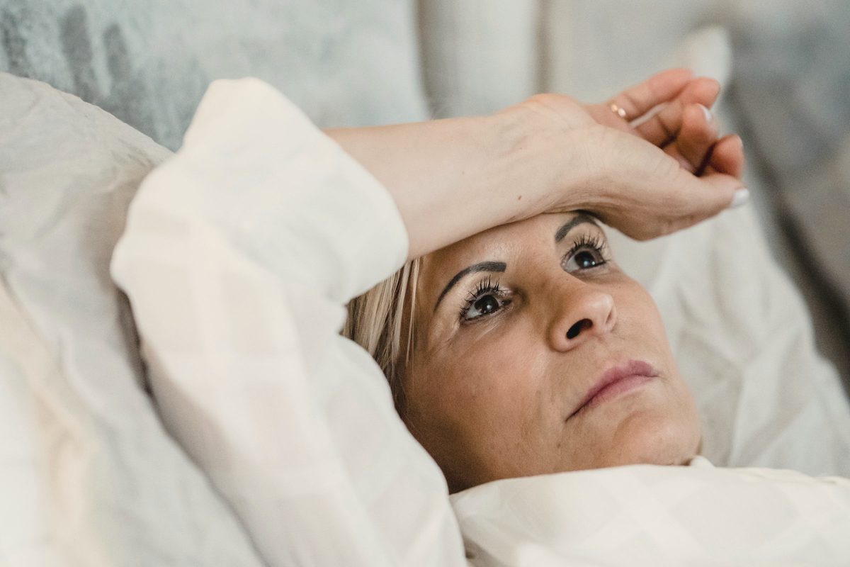 Mature woman lying awake in bed with her hand on her forehead