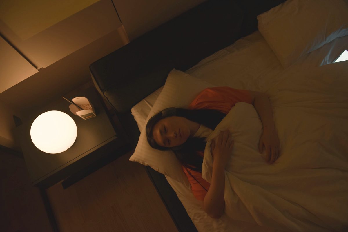 Woman lying in bed at night beside a softly glowing lamp