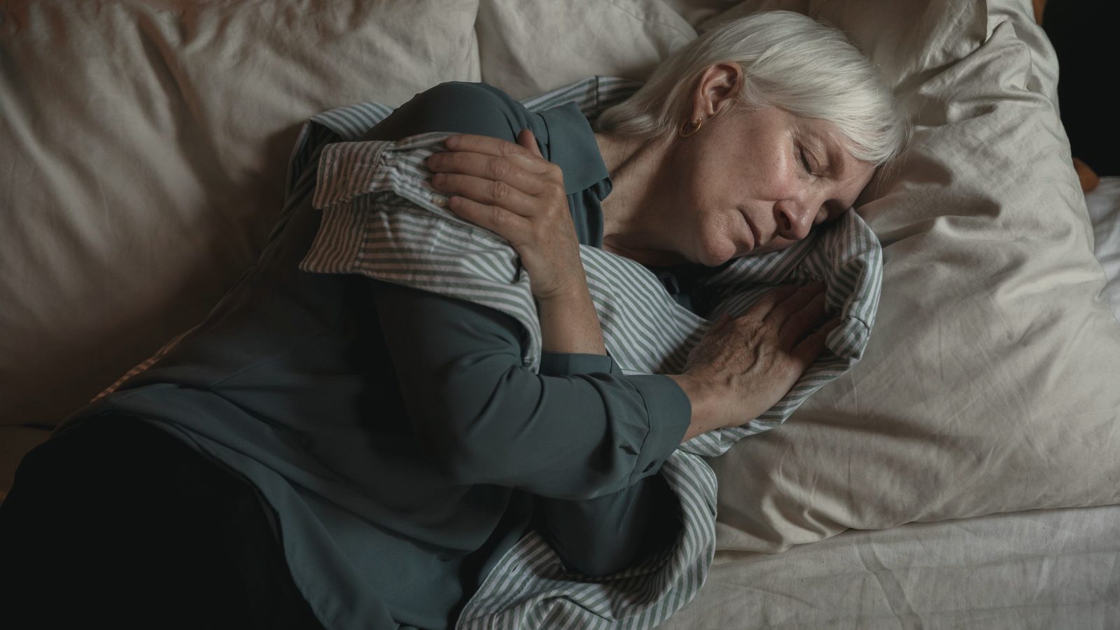 Older woman lying in bed hugging a pillow
