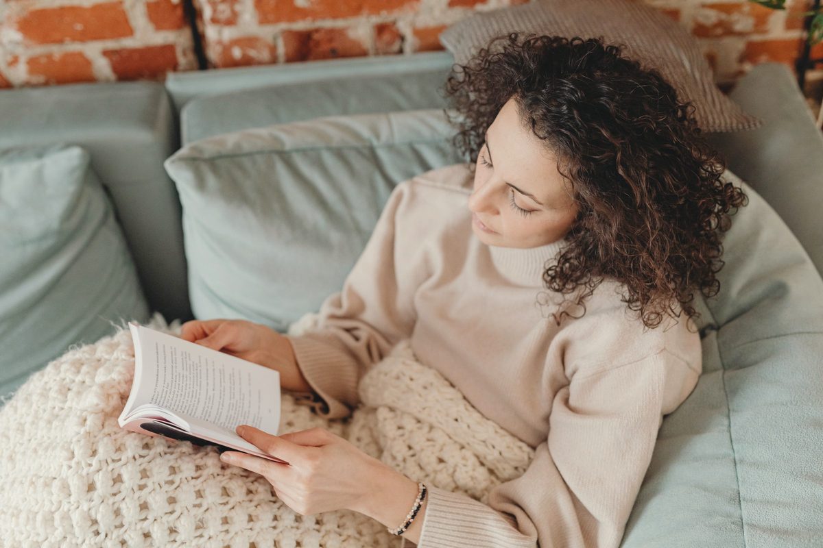 A woman lying on sofa while reading a book