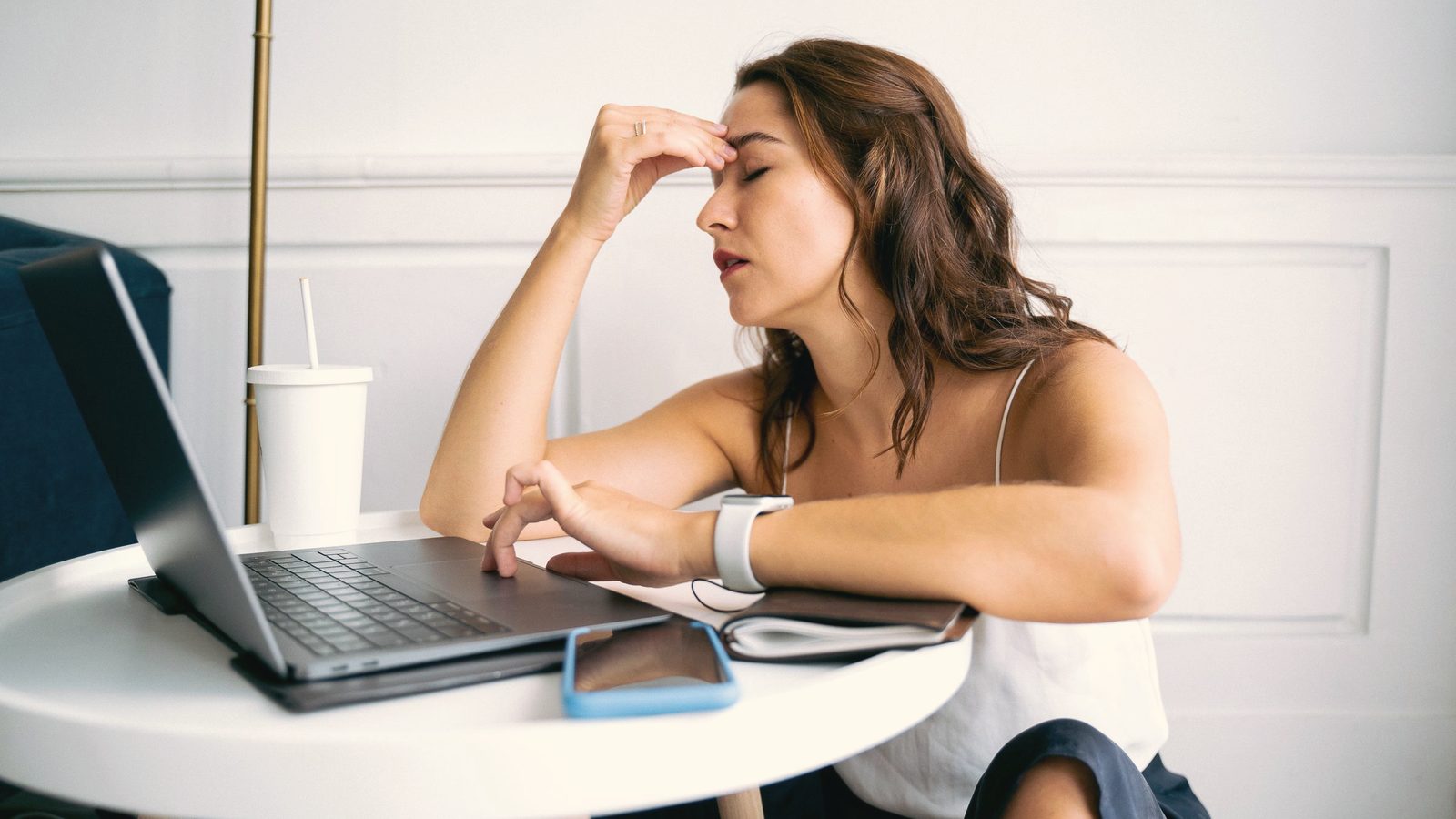 Woman touching her forehead with her eyes closed at her laptop