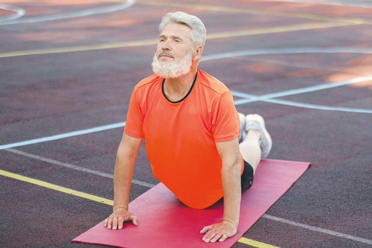 Calm senior man stretching body on stadium