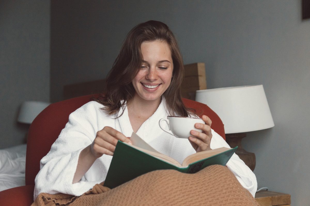 Smiling woman reading in bed with a cup of tea