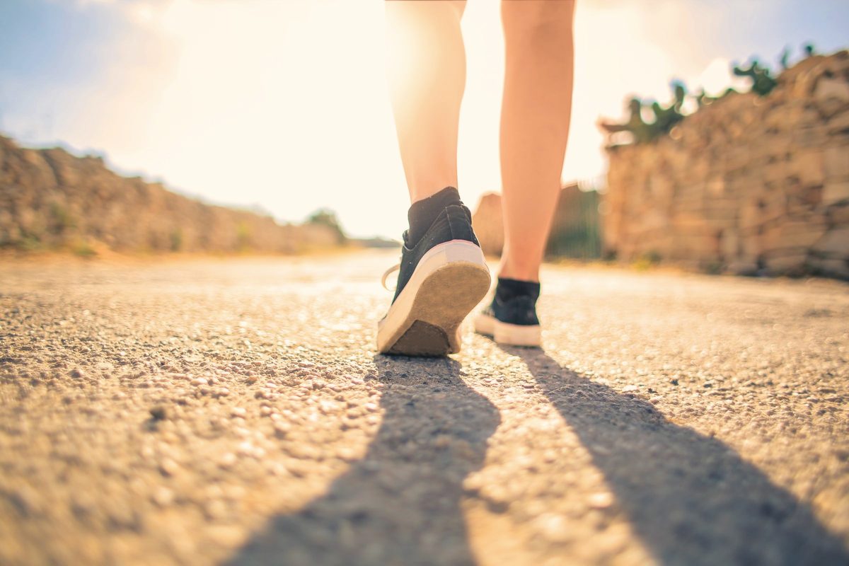 Woman walking on pathway under the sun