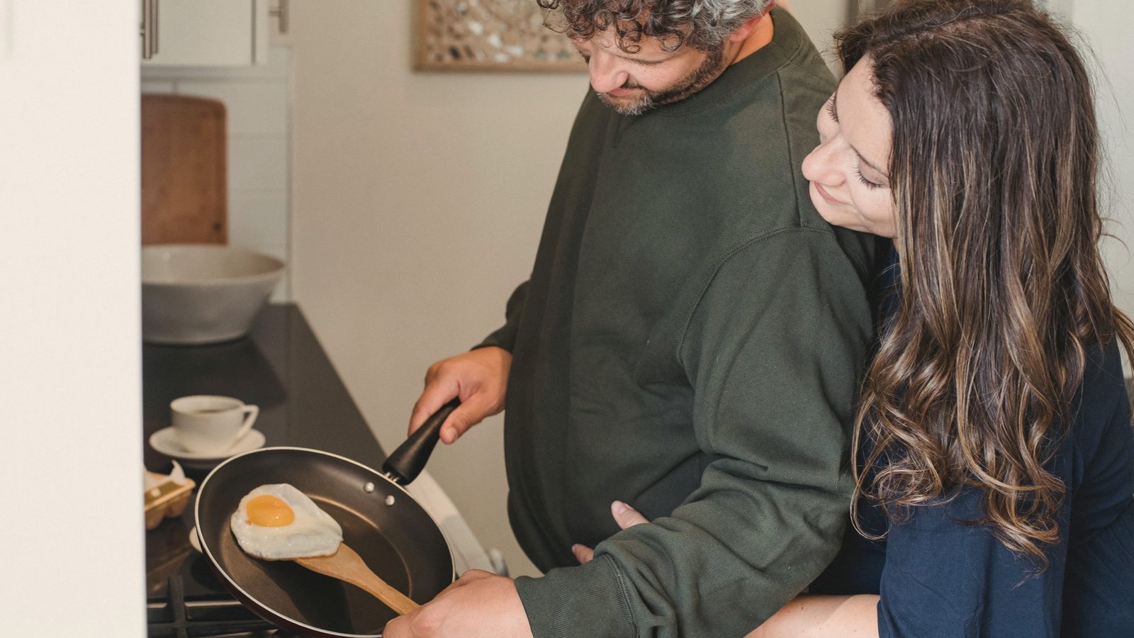 Cheerful couple hugging while cooking eggs for breakfast