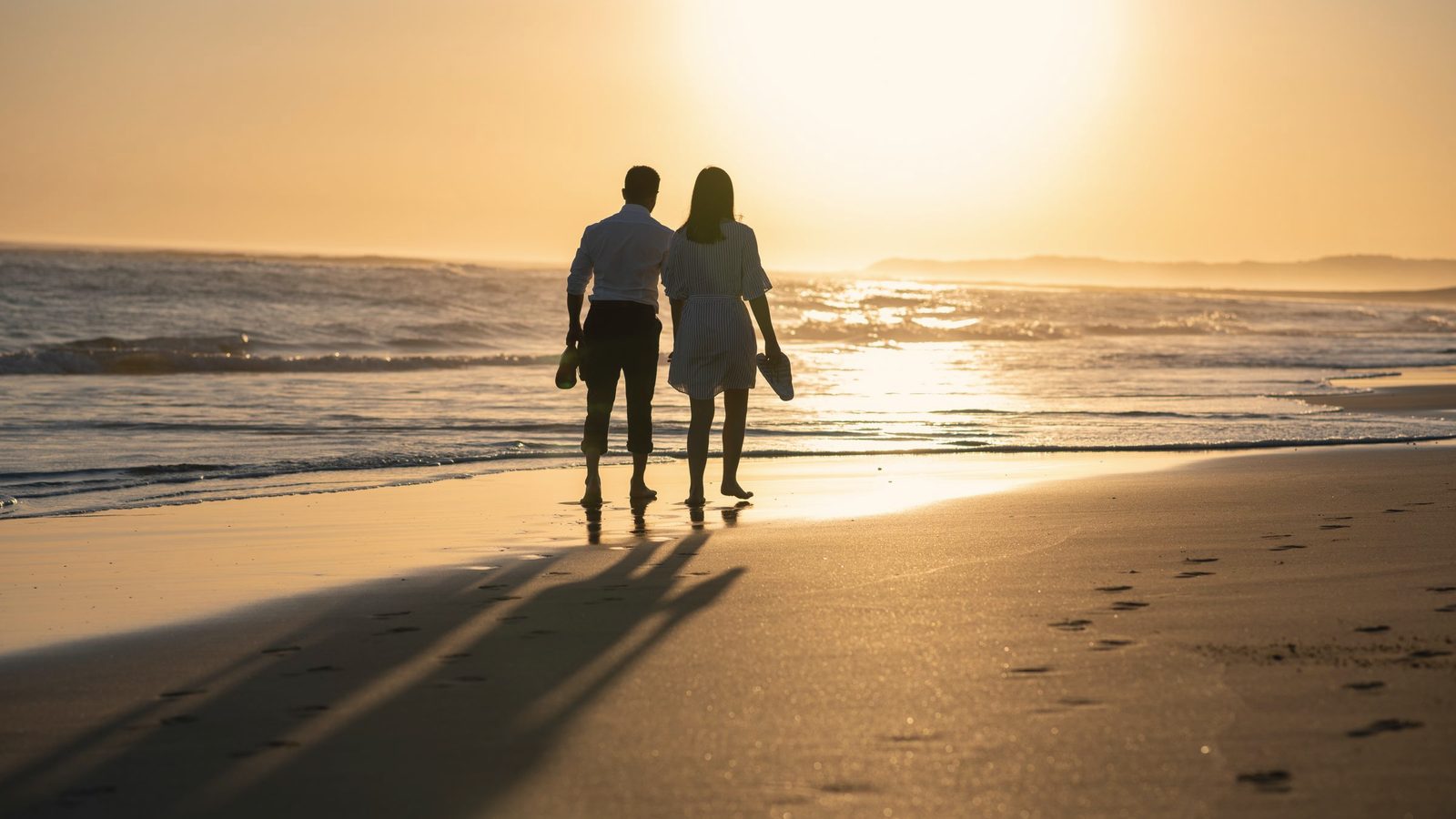 Couple walking slowly along the beach at sunset