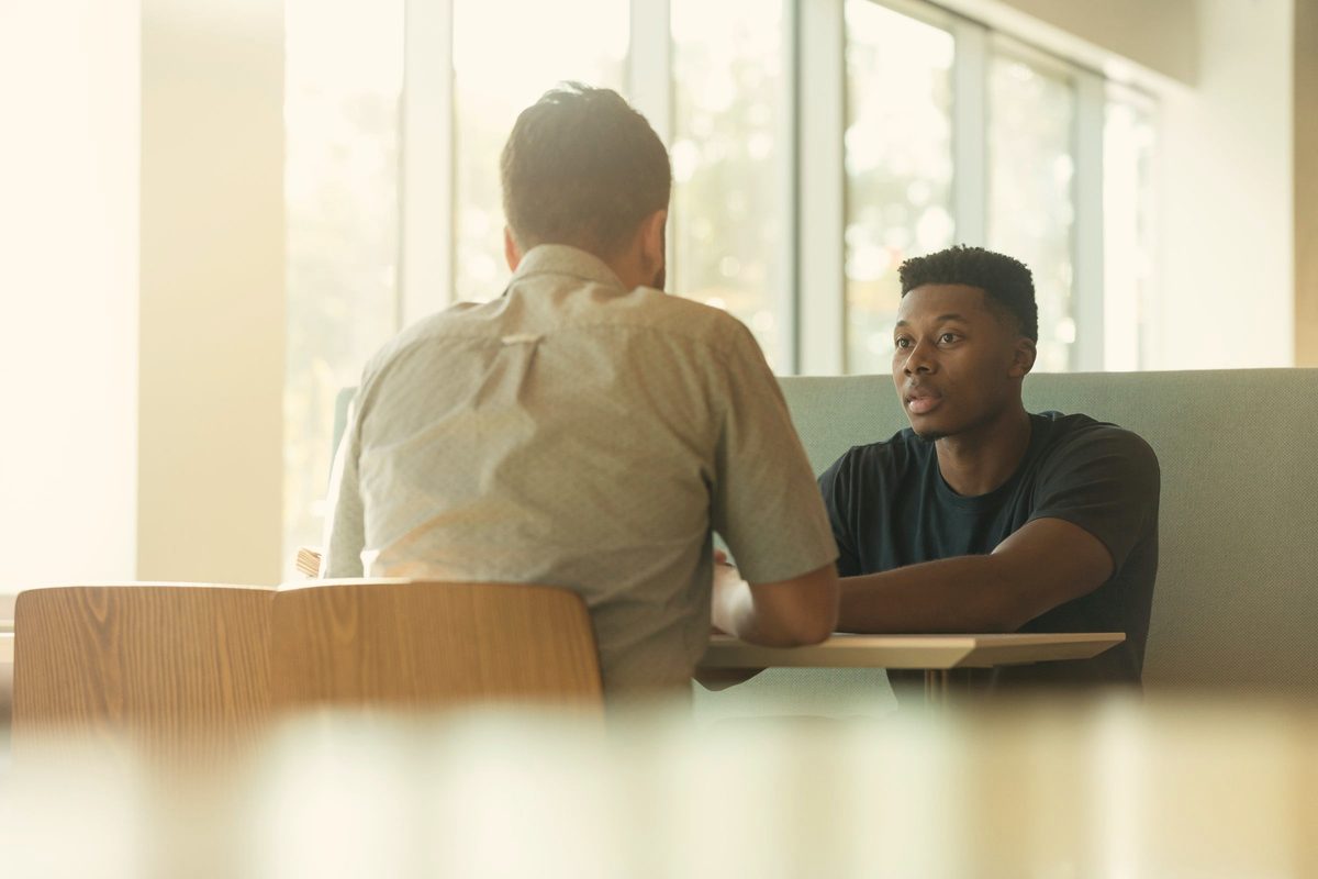Two men talking while sitting beside table