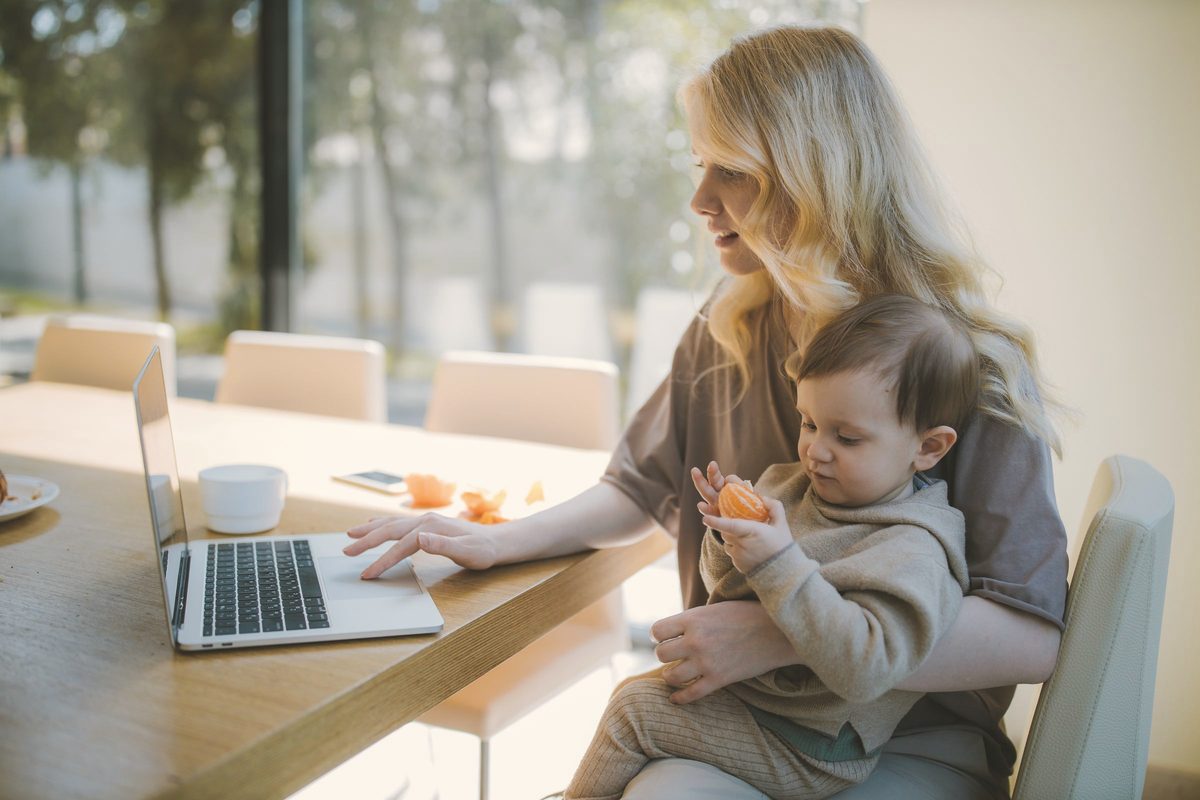 Woman carrying her baby and working on a laptop