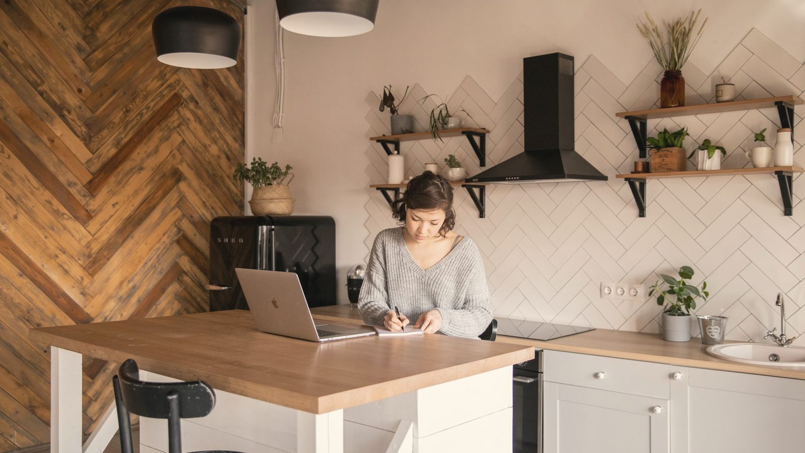 Busy female freelancer with laptop taking notes in kitchen