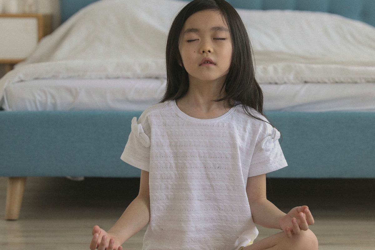 Girl sitting cross-legged with her eyes closed in a bright bedroom